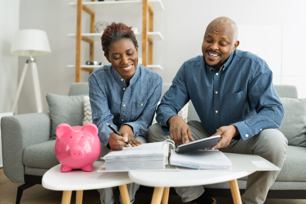 Couple using computer and notebook with a piggybank